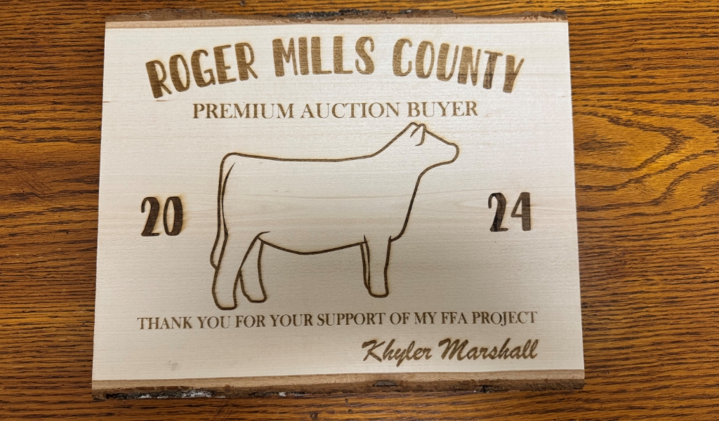 Wooden plaque labeled "Roger Mills County Premium Auction Buyer 2024" with a cow outline and heartfelt thanks from Khyler Marshall for supporting an FFA project.