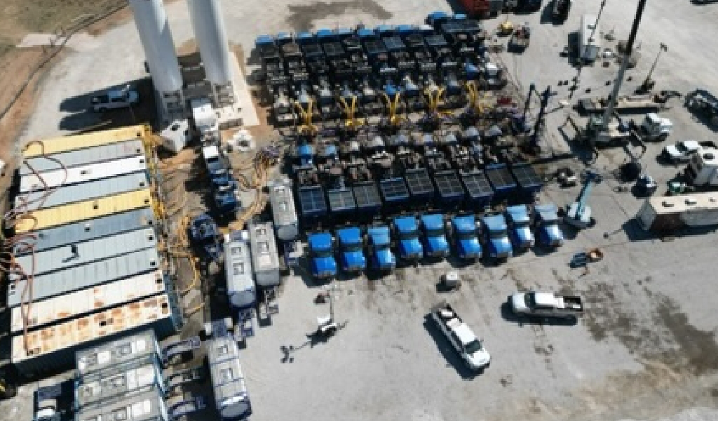 Aerial view of an industrial site with machinery, several trucks, containers, and equipment arranged on a concrete surface.